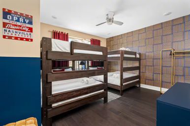 Nashville-themed family bedroom with two dark wood triple bunk beds, geometric patterned accent wall, Music City wall sign, red curtains, ceiling fan and dark hardwood floors.