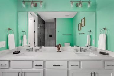 Cheerful mint-green bathroom featuring a white double-sink vanity with chrome faucets, large wall mirror, towel rings, and a glass-enclosed shower