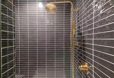 Stylish modern shower with glossy dark gray subway tiles, white grout lines, and brass rain showerhead with matching handheld and controls.