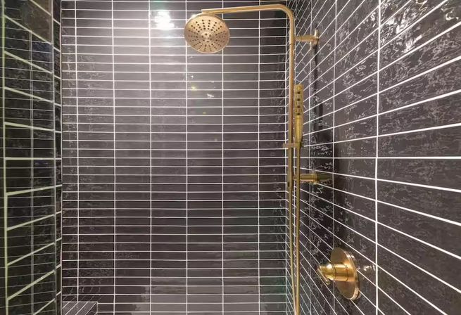 Stylish modern shower with glossy dark gray subway tiles, white grout lines, and brass rain showerhead with matching handheld and controls.
