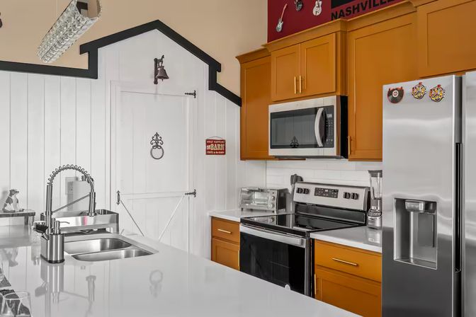 Nashville modern farmhouse kitchen with white shiplap, barn-style door and bell, warm wood cabinets, stainless steel fridge, microwave and range, and a glossy island with dual sink and spring faucet.