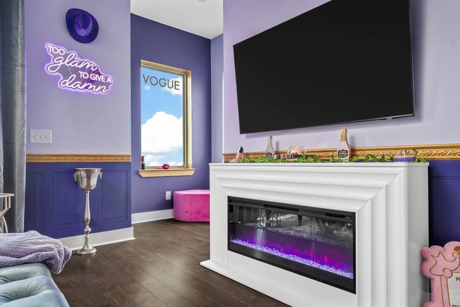 Bright purple living room with a wall-mounted TV above a white electric fireplace glowing pink, neon 