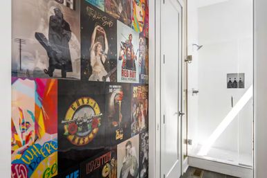 White modern bathroom with glass-enclosed shower and a bold, colorful collage of vintage rock album cover posters on the adjacent wall.