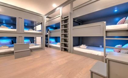 Modern sleep room with built-in gray bunk beds, white linens, blue LED accent lighting and light wood floors — cozy dorm-style bunk room for groups.