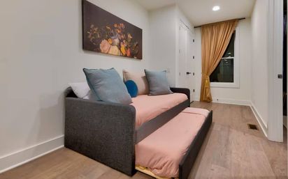 Cozy modern guest room with a gray trundle sofa bed and blush-pink bedding, blue accent pillows, floral wall art, hardwood floors, white walls and a mustard-gold curtain over the window