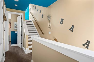 Cheerful modern home stairway with white wooden steps, teal ceiling accent, beige walls decorated with metal letters and a small windmill, and dark hardwood floor