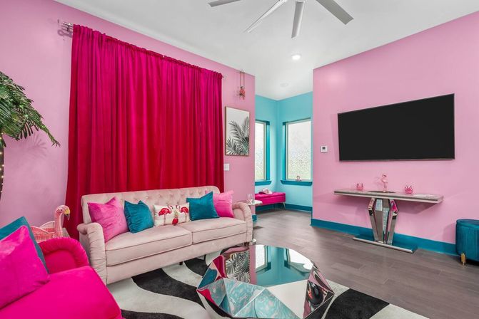 Vibrant pink living room with fuchsia curtains, tufted blush sofa with teal pillows, mirrored geometric coffee table, teal trim and wall-mounted TV