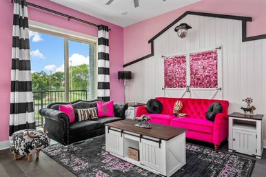 Vibrant pink living room with hot-pink tufted sofa, black velvet Chesterfield couch, black-and-white striped curtains, farmhouse coffee table and pink mosaic barn-door wall art