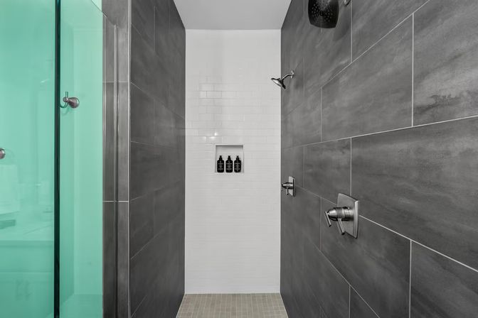 Modern walk-in shower with dark gray large-format tiles, white subway-tile niche holding shampoo bottles, brushed steel shower fixtures and glass door
