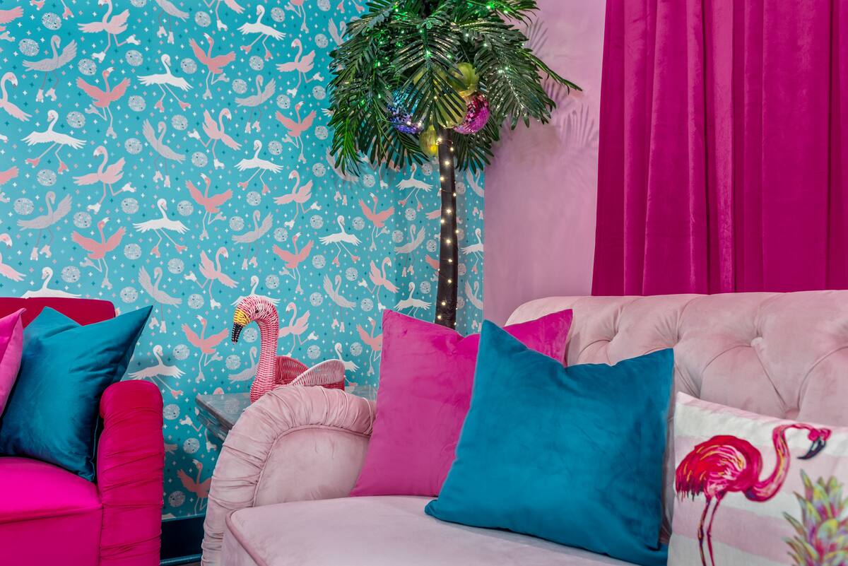 Vibrant tropical living room with turquoise flamingo wallpaper, pink velvet sofa, teal and magenta pillows, lit faux palm and flamingo decor