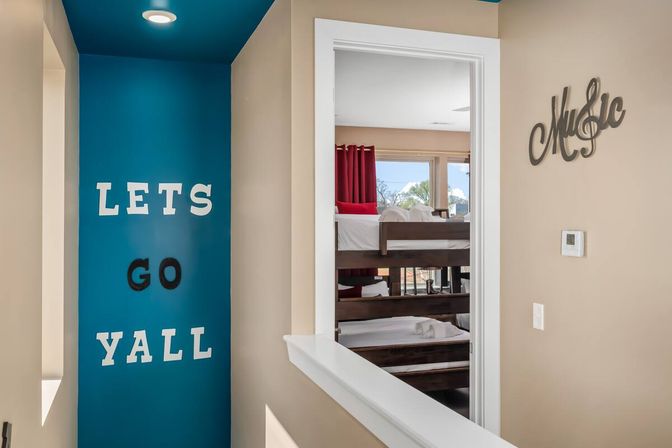 Bright hallway with teal accent wall reading "LETS GO YALL," open doorway to a bedroom with wooden bunk beds, red curtains and white bedding in a family-friendly vacation rental interior.