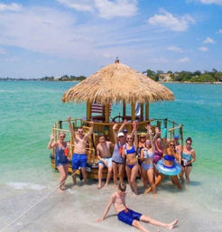 Group of people in swimsuits waving from a thatched-roof floating tiki raft beached on a sunny tropical shoreline with clear turquoise water.