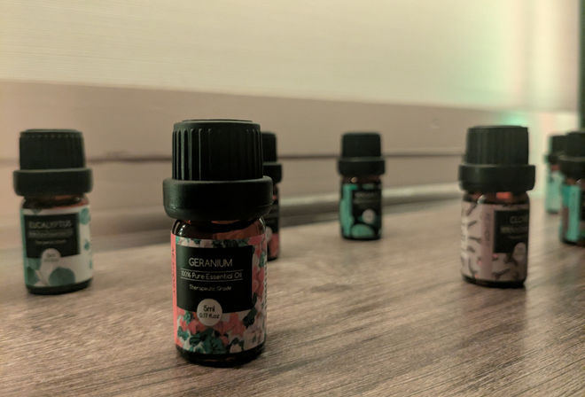 Close-up of small amber essential oil bottles on a wooden surface, foreground focus on a 5ml geranium essential oil bottle with a floral label and blurred bottles in the background.