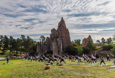 Outdoor yoga class on a grassy field in front of towering red-rock formations under a dramatic cloudy sky