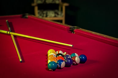 Red-felt pool table with racked colorful billiard balls and two crossed cues, ready for a game night in an indoor game room.
