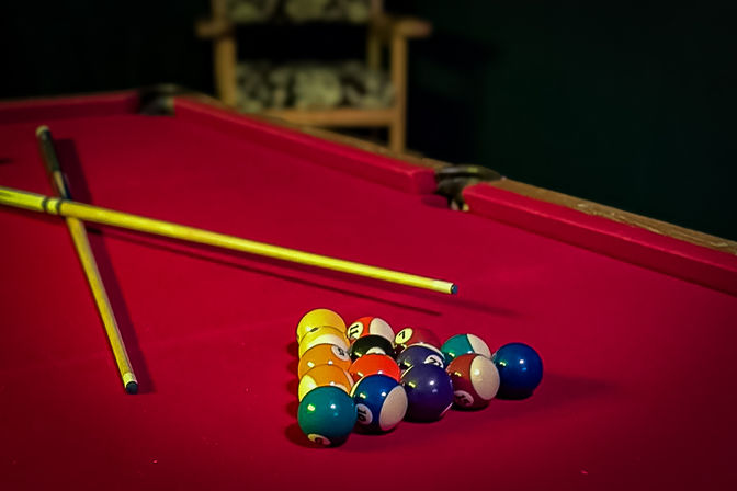 Red-felt pool table with racked colorful billiard balls and two crossed cues, ready for a game night in an indoor game room.