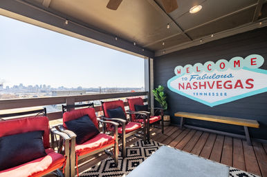 Covered rooftop patio in Nashville, Tennessee with red-cushioned chairs, black-and-white rug, wooden decking, skyline view, and a playful "Welcome to Fabulous Nashvegas Tennessee" wall mural.