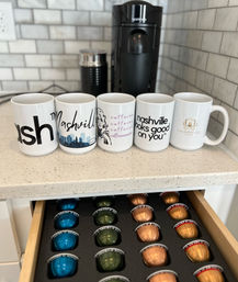 Kitchen coffee station with five Nashville-themed mugs lined up in front of a black pod coffee machine and an open drawer of colorful coffee capsules.