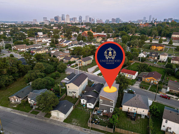 Aerial shot of a residential neighborhood with the downtown skyline in the distance and a large red location pin with a decorative crest highlighting a two-story house.