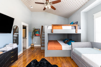 Cozy modern bunk-bedroom with gray built-in bunk beds and orange bedding, single daybed, hardwood floors, patterned vaulted ceiling with ceiling fan, wall-mounted TV and dresser