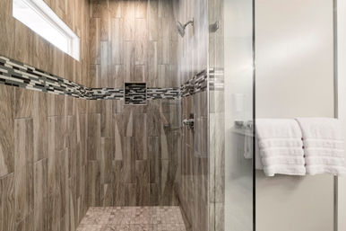 Modern walk-in bathroom shower with wood-look tile walls, horizontal mosaic accent band, recessed niche, glass door and folded white towels
