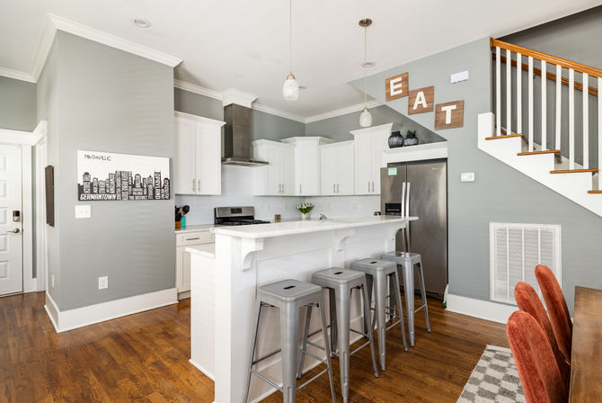 Bright modern kitchen in a Nashville home — white cabinets, marble-look island with four metal bar stools, stainless appliances, gray walls and hardwood floors.