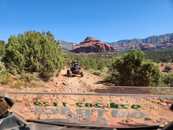 UTV on a rocky desert trail with red sandstone buttes, scrubby juniper and a clear blue sky — off‑road adventure in a southwestern red‑rock landscape