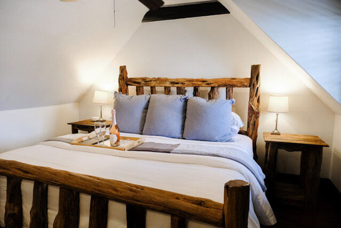 Cozy rustic attic bedroom with a log-frame bed, white linens and soft gray pillows, bedside tables and lamps, and a champagne tray on the bed
