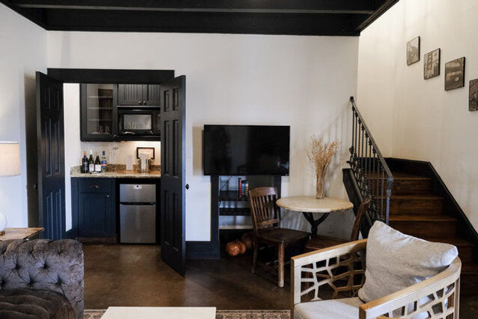 Cozy urban loft living area with small kitchenette, wall-mounted TV, round bistro table, and wooden staircase