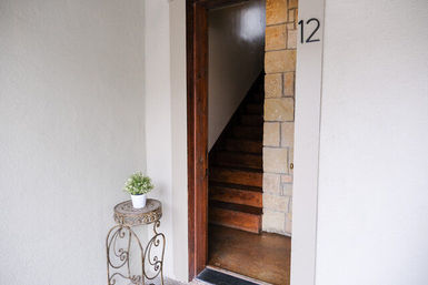 Open entryway marked 12 showing wooden staircase and stone-trimmed wall, with a small potted plant on a decorative wrought-iron stand by the door