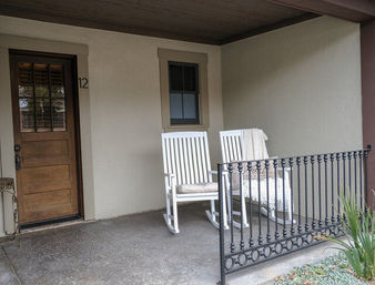 Cozy residential front porch with a wooden entry door, two white rocking chairs (one with a knit throw) and decorative iron railing