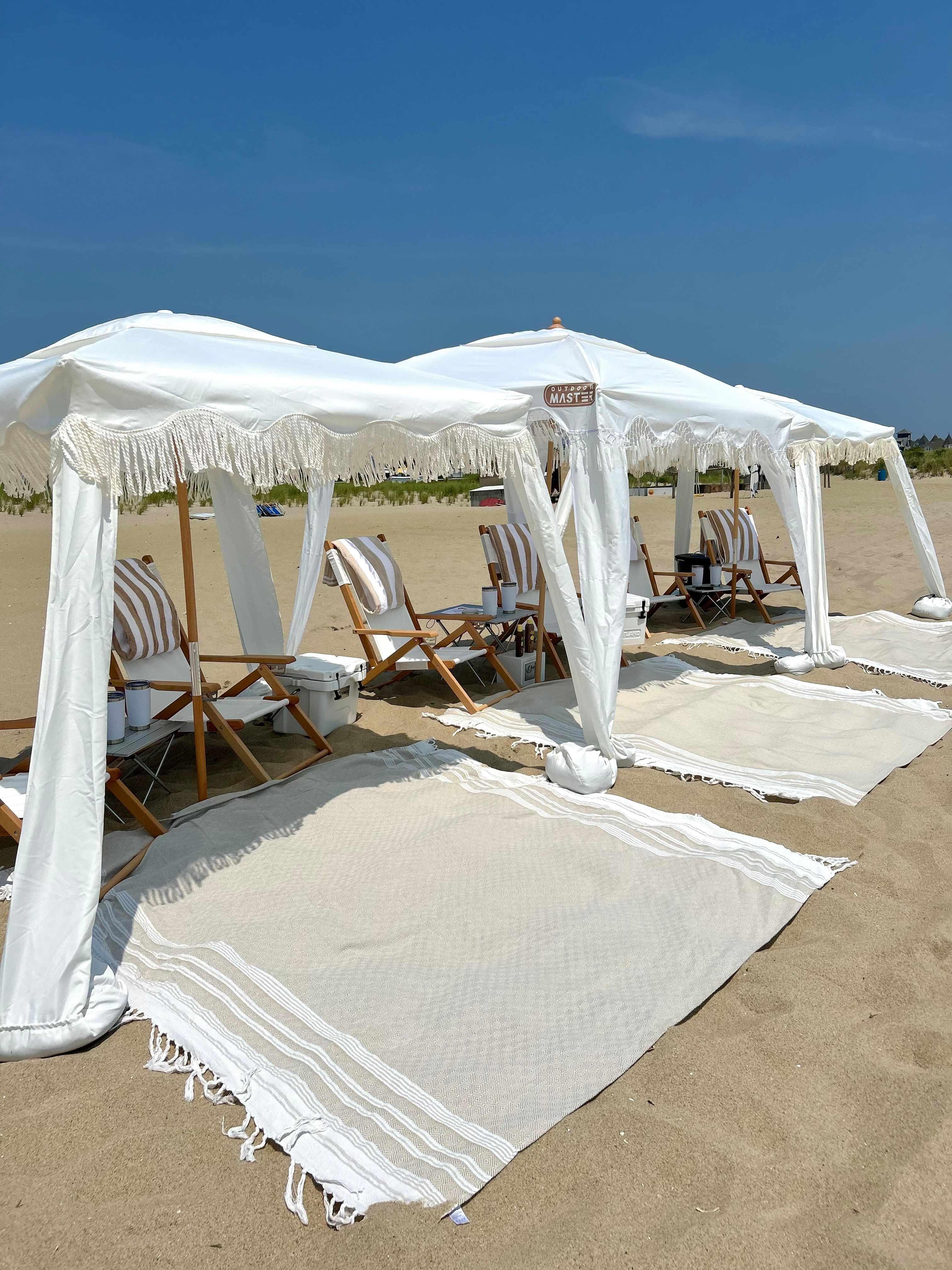 Sunny seaside scene with white fringe canopies and striped wooden lounge chairs set on sandy shore under a clear blue sky