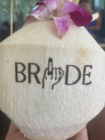 Close-up of a hand-held shaved young coconut topped with a bright pink orchid petal and a burned brand mark on the shell, tropical drink garnish