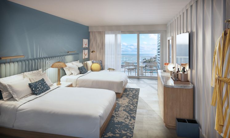 Modern oceanfront hotel room with two beds, blue accent wall, coastal decor, TV and balcony seating overlooking the sea.