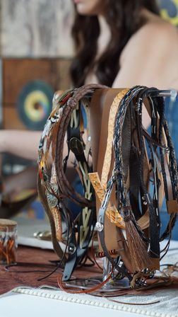 Close-up of handmade leather headbands, braided straps and feathered boho accessories hanging on a display rack at an artisan market