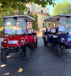 Two festive red and blue golf carts with star-spangled tinsel parked under trees in a sunny Scottsdale courtyard with Spanish-style buildings