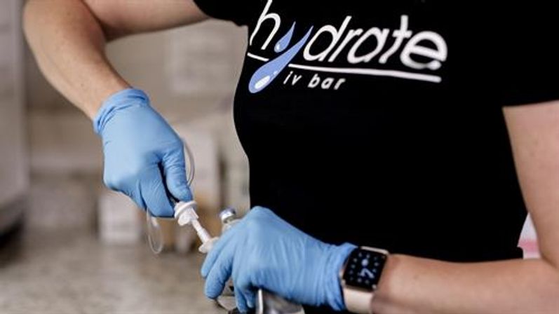 Close-up of gloved hands prepping an IV drip and tubing at a hydration wellness clinic, technician loading fluid into a syringe.