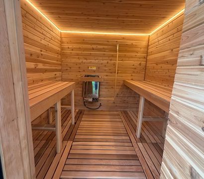 Modern cedar sauna interior with parallel wooden benches, slatted floor, wall-mounted heater and warm LED cove lighting.