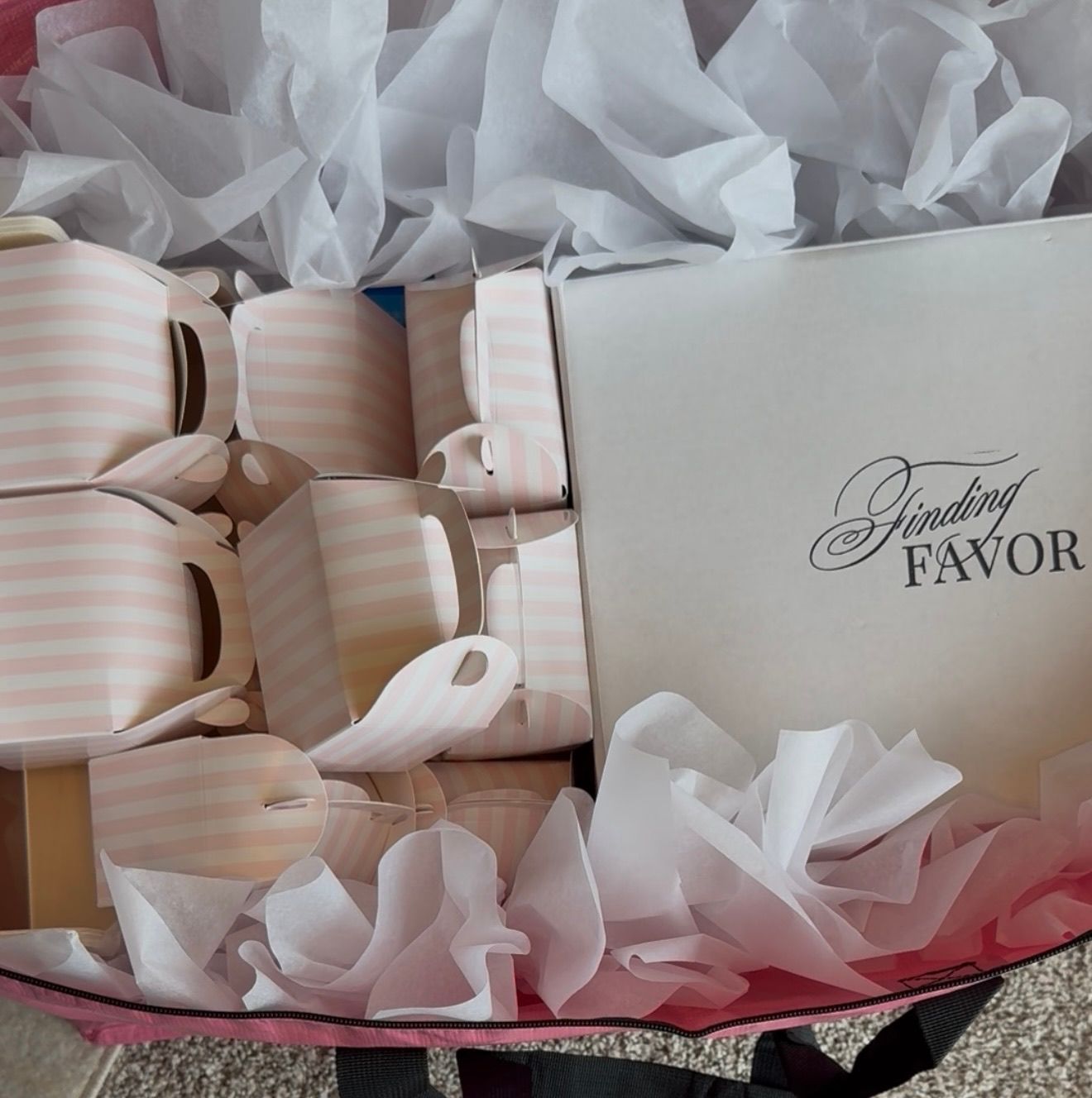 Pink-and-white striped mini bridal favor boxes arranged in a gift box, nestled in crinkled white tissue paper beside a white lid with cursive lettering.