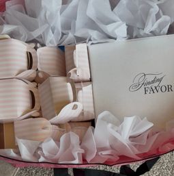 Pretty pink-and-white striped party favor boxes nestled in white tissue paper next to a white box with decorative script, perfect for bridal shower or wedding favors.