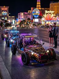 Neon-lit open-frame buggies cruising the Las Vegas Strip at night with bright casino lights and onlookers snapping photos