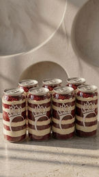 Six clear cans of layered red velvet cake and cream — cake-in-a-can desserts with pull-tab lids and crown motif — arranged on a marble countertop against a neutral textured wall.