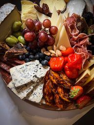 Gourmet charcuterie board with blue cheese slices, aged cheese wedges, folded prosciutto and spicy salami, red grapes, green olives, roasted red peppers, blueberries, figs and almonds on a wooden platter