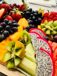 Colorful fresh fruit platter with sliced dragon fruit, kiwi, cantaloupe, honeydew, grapes, strawberries and raspberries — vibrant tropical fruit tray for brunch or catering