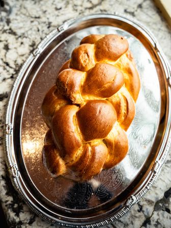 Freshly baked golden braided challah loaf on an ornate silver platter atop a speckled stone countertop