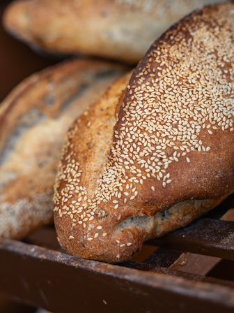 Close-up of a freshly baked artisan sesame seed loaf with a golden crust resting on a wooden bakery rack