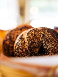 Close-up of a fresh poppy seed bagel with golden crust and dense black seeds in a bakery basket, appetizing breakfast pastry