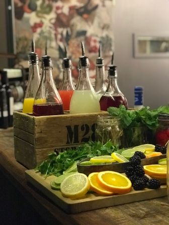 Cocktail garnish station with glass pourer bottles of colorful mixers in a wooden crate, sliced lemons, limes and oranges, blackberries and fresh herbs