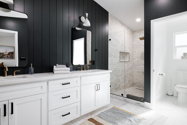 Sleek modern bathroom with black vertical accent wall, white double vanity and brass faucets, marble tile floors and a glass walk-in shower