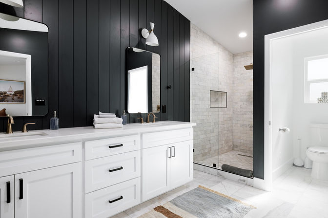Sleek modern bathroom with black vertical accent wall, white double vanity and brass faucets, marble tile floors and a glass walk-in shower